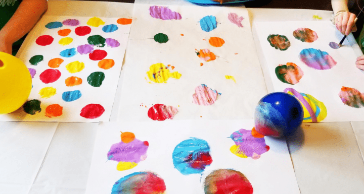 Kid stamping colourful paint on paper using balloons